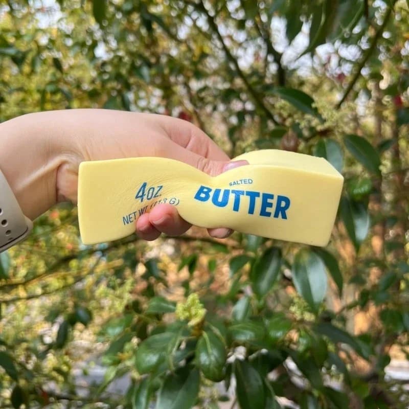 A hand squeezing a realistic-looking yellow butter stick fidget toy outdoors.