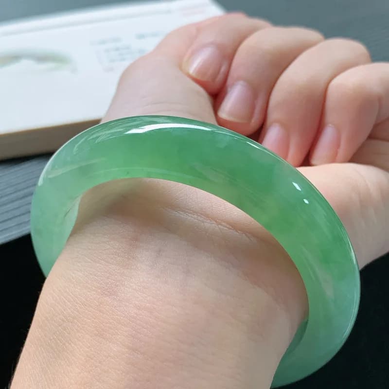 Translucent green Burmese ice waxy jadeite bracelet with floating patterns worn on a wrist.