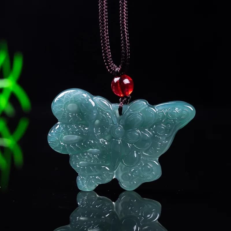 Intricately carved blue water ice type natural jadeite butterfly pendant on a dark cord with a red accent bead.
