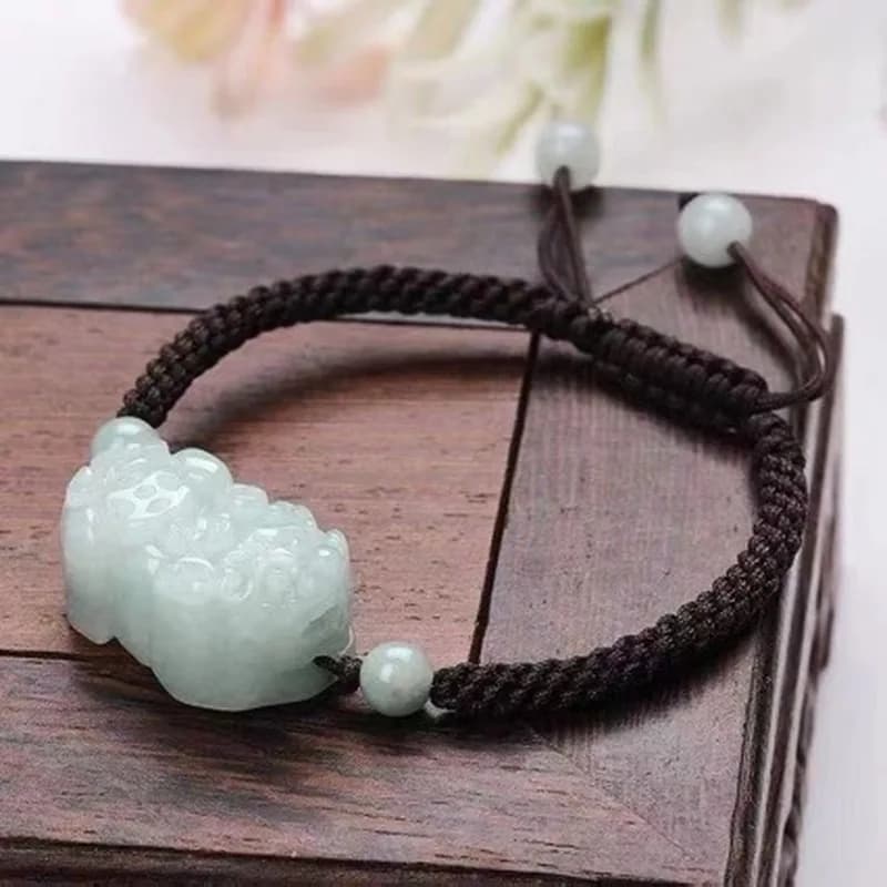 A hand-carved light green jadeite Pixiu charm on a dark braided cord bracelet.
